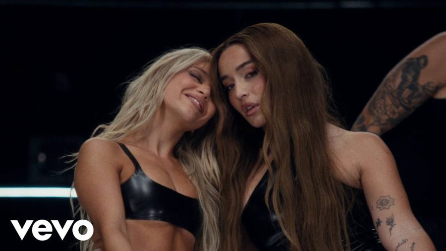 canciones-de-lola-indigo | Slow Radio Two women with long hair in black outfits lean together and smile, on stage with a Vevo watermark in the corner.