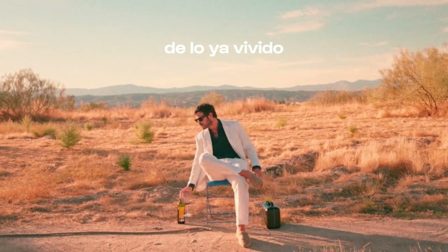Canciones-de-Taburete | Slow Radio Man in a white suit sits on a chair in a desert, holding a bottle; a second bottle and a jug nearby; overlay text 'de lo ya vivido'.